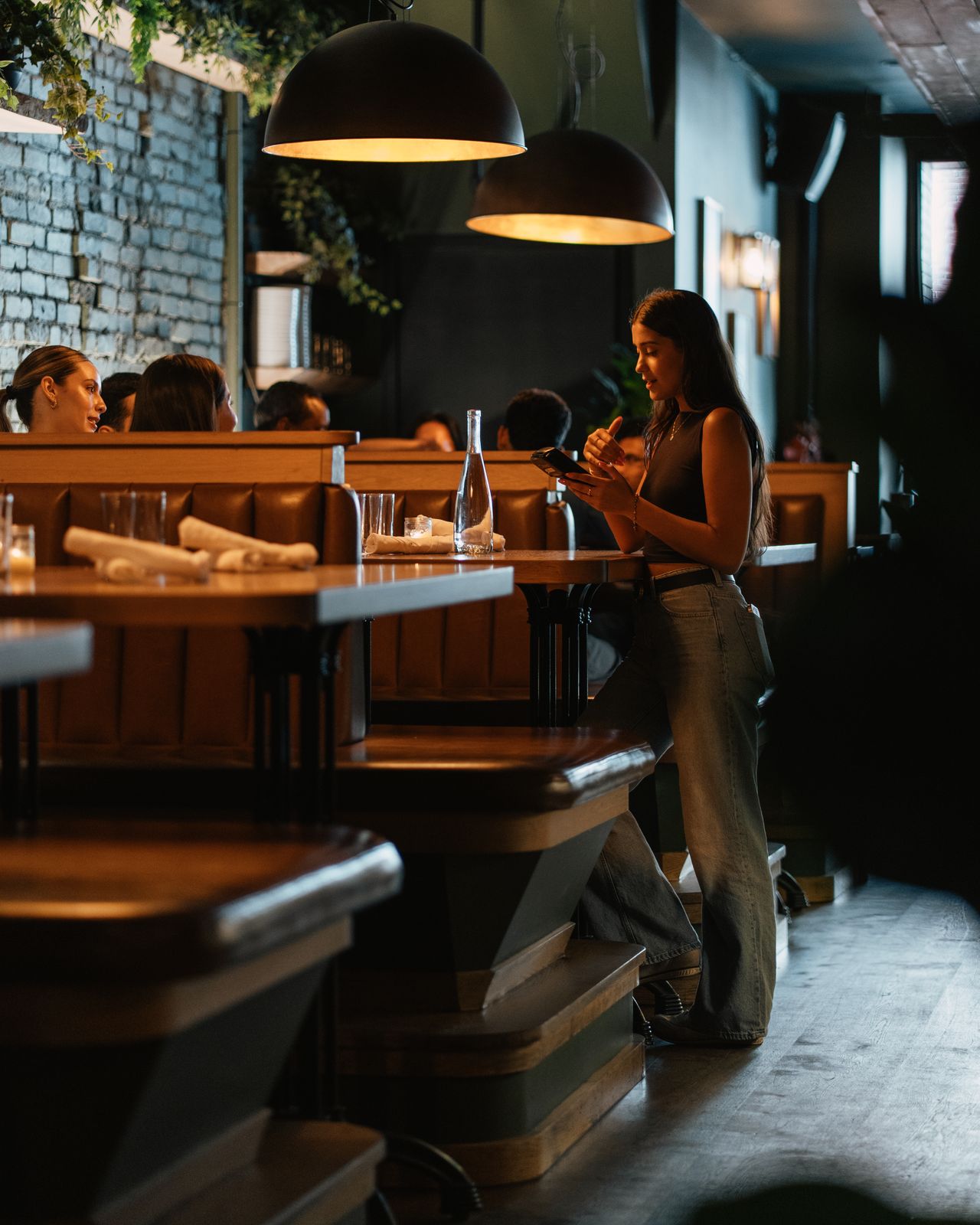 A guest checking her phone in Dear Maud's dim, warmly lit dining room in the evening