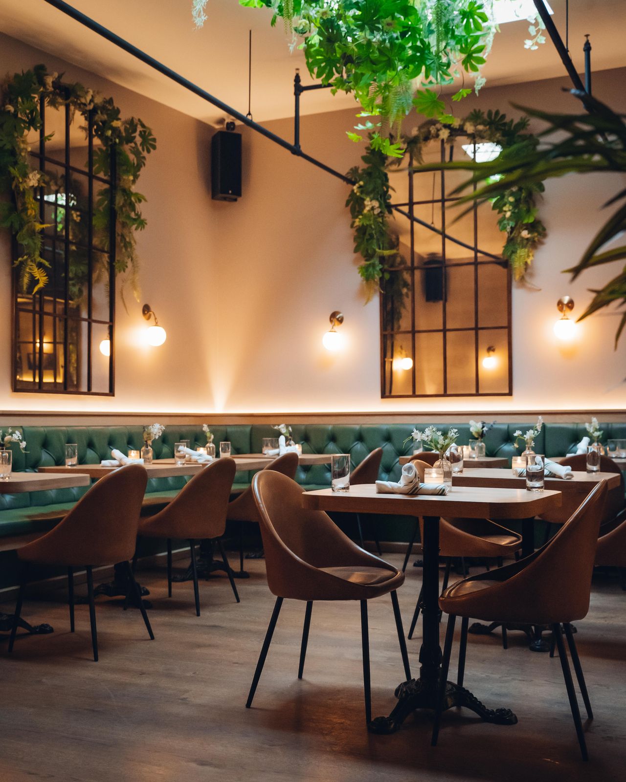 Dear Maud's dining room, with hanging greenery, mirrored window frames, and warm sconce lighting