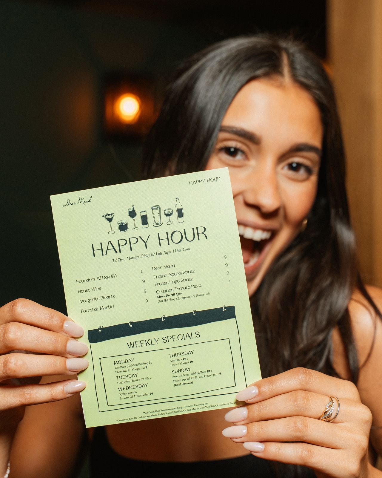 A guest holding up Dear Maud's happy hour menu card