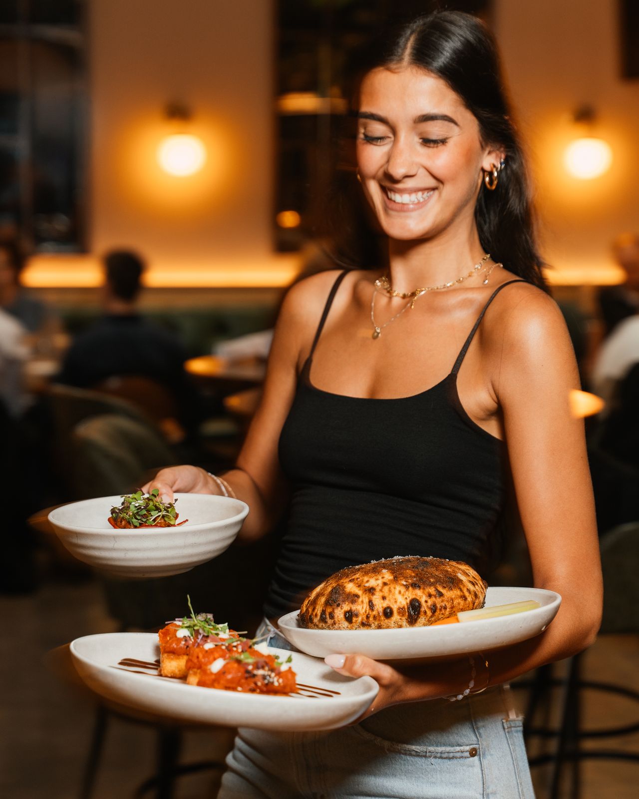 A server carrying plates of steak bites and short rib fried rice through Dear Maud's dining room